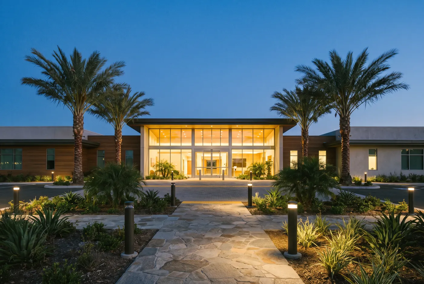 Medical centre entrance glowing at dusk behind palm trees