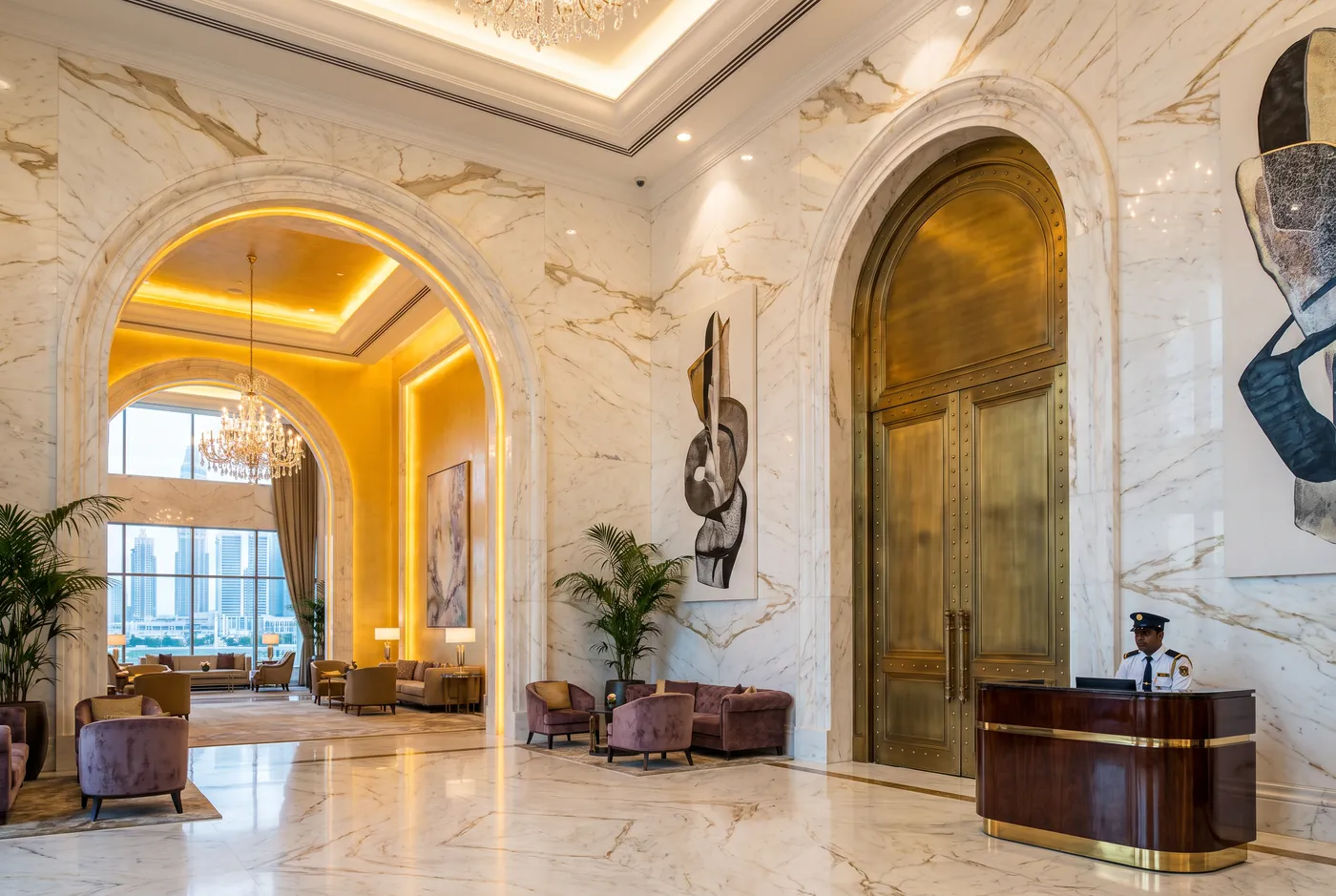 Marble hall with one open arched doorway and one closed brass door beside a security desk