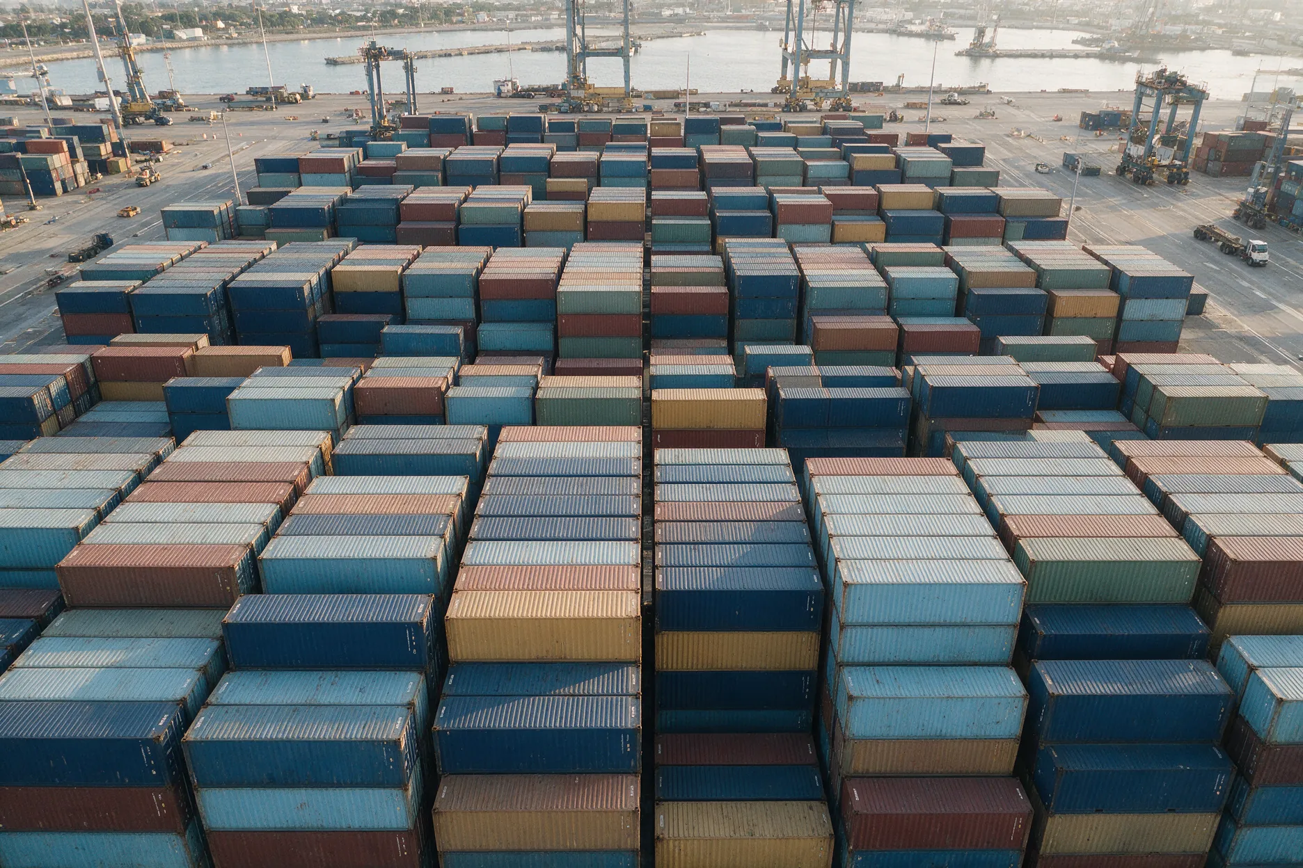 Aerial view of neatly stacked shipping containers in muted colours at a port terminal